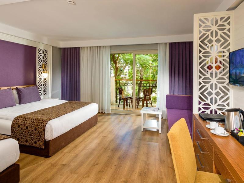 Chambre d'hôtel moderne avec parquet, lit double, terrasse et télévision murale.