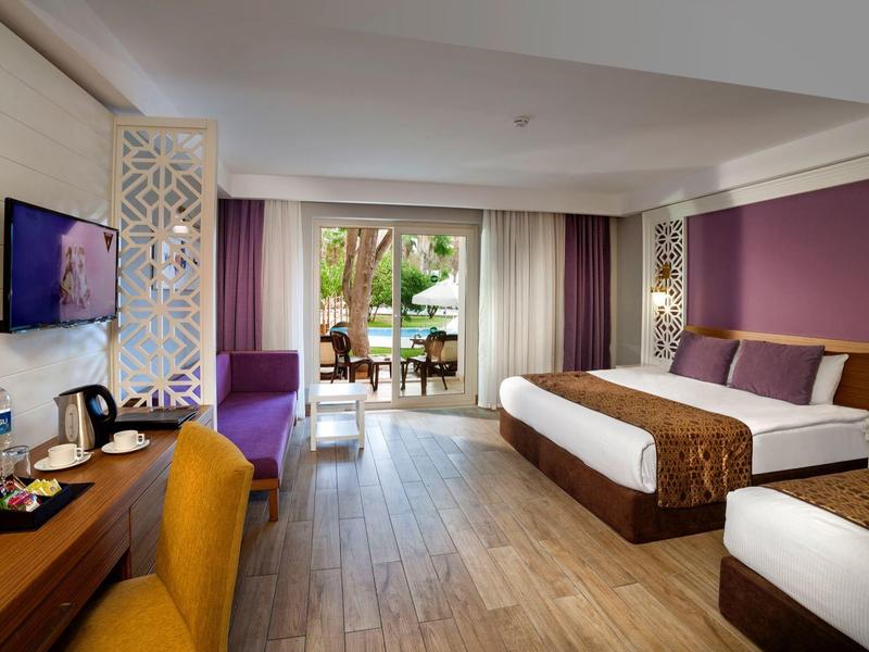 Chambre d'hôtel spacieuse avec deux lits, bureau, chaise jaune et vue sur un jardin.