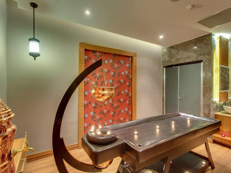 Salle de spa avec table de massage, porte rouge, lumière tamisée et déco chaleureuse.