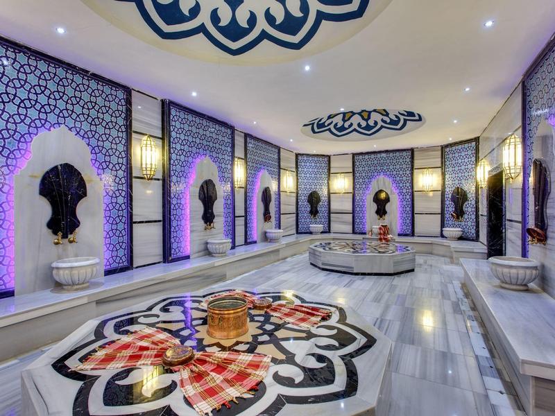 Intérieur luxueux d'un hammam avec décorations murales et fontaines éclairées.