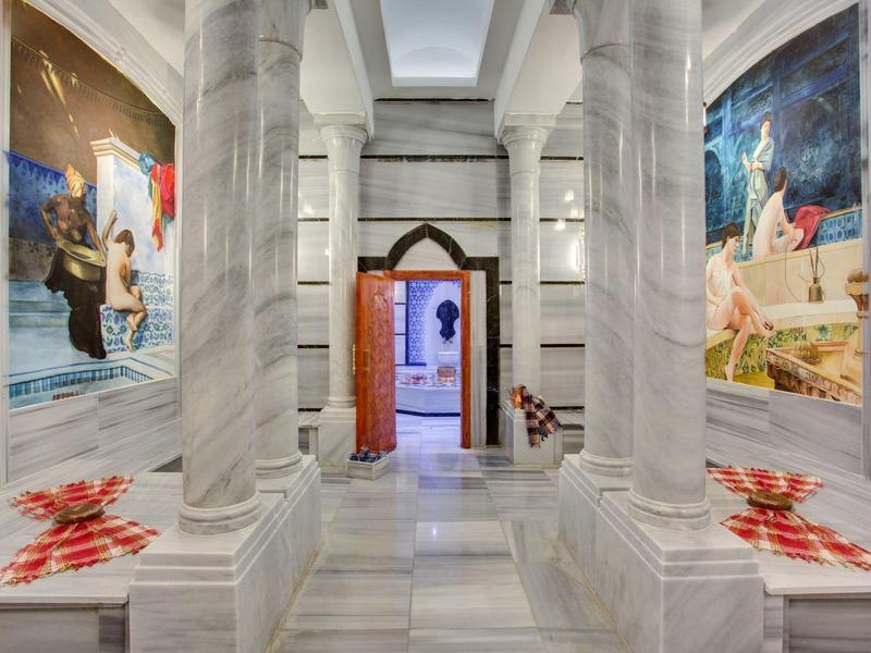 Intérieur de hammam en marbre blanc avec grandes colonnes et décorations murales colorées.