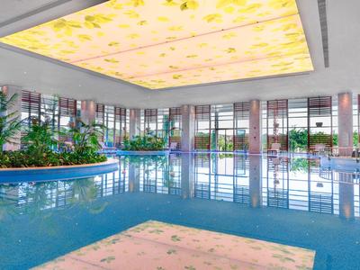 Overdekt hotelzwembad met helder water, omgeven door planten en grote ramen.