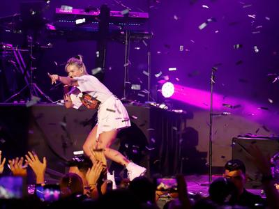 An artist poses at a concert in front of a cheering crowd, surrounded by confetti.