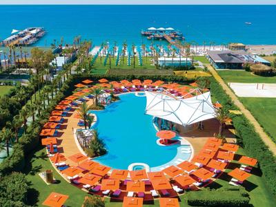 Een rond zwembad met oranje ligstoelen en parasols met uitzicht op zee en aanlegsteigers.