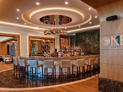 Moderne hotelbar met cirkelvormige plafondverlichting, houten accenten en comfortabele zitplaatsen.