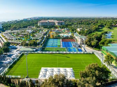 Blick auf Fußballfelder und Tennisplätze neben einem Hotelkomplex umgeben von Grünflächen.