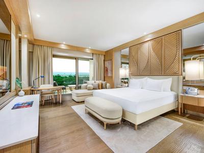 Helles Hotelzimmer mit großem Bett, Sitzbereich und Panoramafenstern mit Aussicht.
