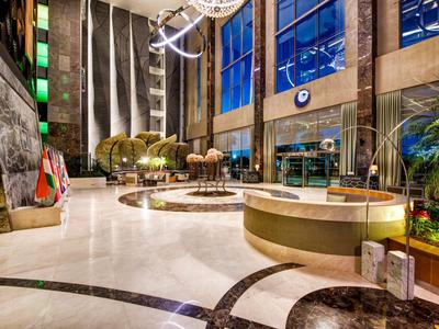 Helle Hotellobby mit hohem Glasfenster, moderner Beleuchtung und dekorativen Pflanzen.