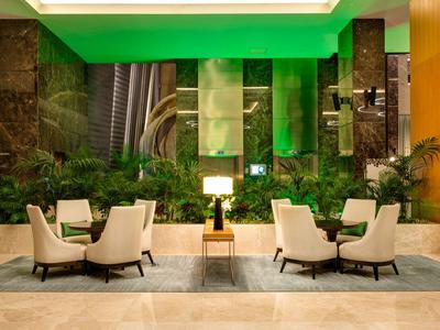 Moderne Hotellobby mit bequemen Sesseln, grüner Beleuchtung und Pflanzen.