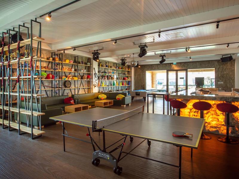 Moderne lounge met kleurrijke planken, zitplaatsen en tafeltennistafel onder helder licht.