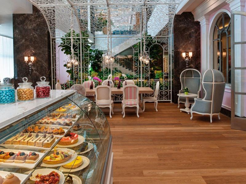 Elegante bakkerijcafé met houten vloer, glazen vitrinekast met gebak en comfortabele zitplaatsen.