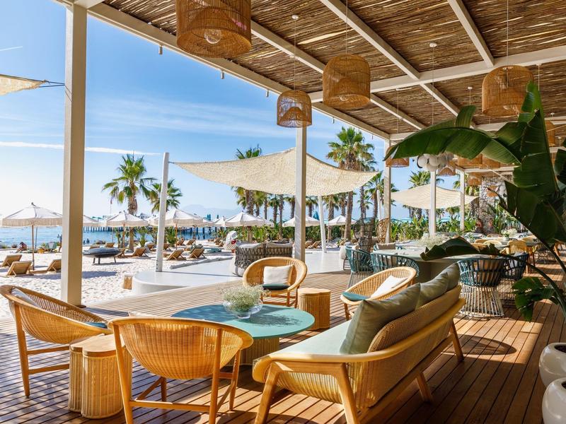 Buitenlounge bij een strandresort met houten meubels en zeezicht onder een overdekt dak.