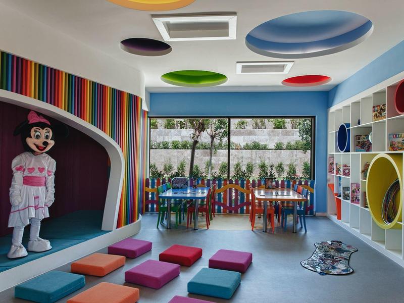 Kleurrijke speelkamer voor kinderen met kussens, klimframe en cartoonfiguur.