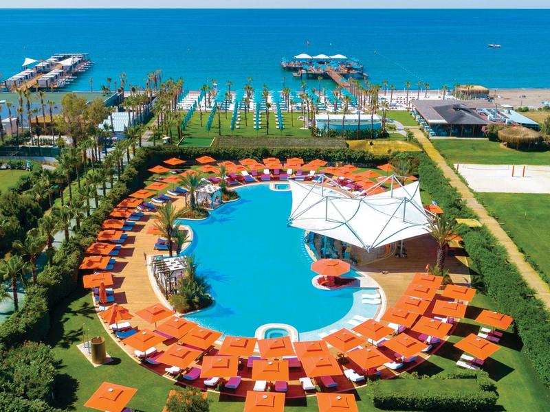 Een rond zwembad met oranje ligstoelen en parasols met uitzicht op zee en aanlegsteigers.
