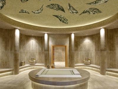 Round spa with central pool, marble walls, and ceiling decorated with leaf motifs.