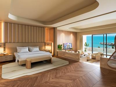 Elegant hotel room with large bed, seating area, and sea view through large windows.