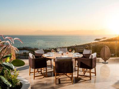 Area pranzo all'aperto con tavolo e sedie con vista sul mare al tramonto.