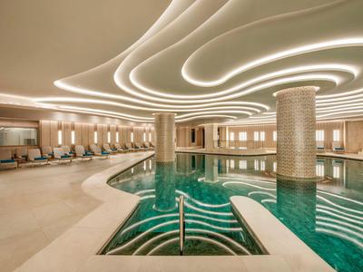 Area interna dell'hotel con piscina curva moderna e illuminazione indiretta sul soffitto.