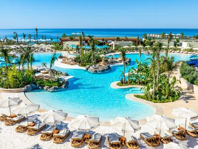 Grande piscina dell'hotel con piante tropicali, lettini e vista sul mare.