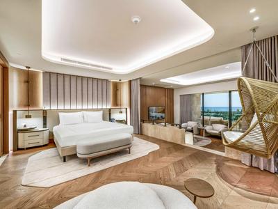 Camera d'hotel elegante con letto grande, poltrona, tappeto e vista sul mare e sul giardino.