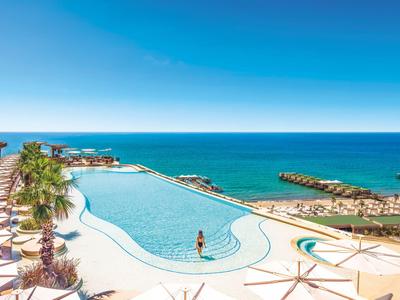 Piscina moderna con piattaforma panoramica e vista mare in una giornata di sole.
