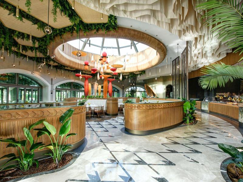 Spacious hotel lobby with tropical decor and a hanging Santa Claus under a glass roof.