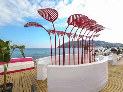 Opera d'arte rossa su una terrazza in legno con vista mare e cielo azzurro.