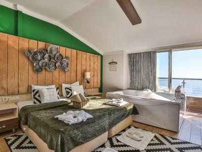 Camera d'hotel luminosa con parete in legno, letto matrimoniale, divano e grande finestra con vista mare.