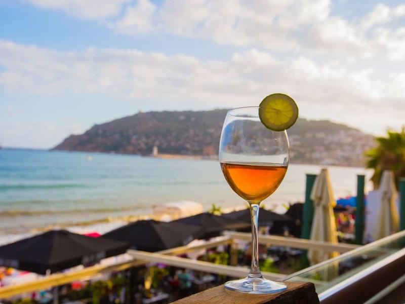 Bicchiere di vino con fetta di lime davanti alla spiaggia, al mare e alla collina sullo sfondo.