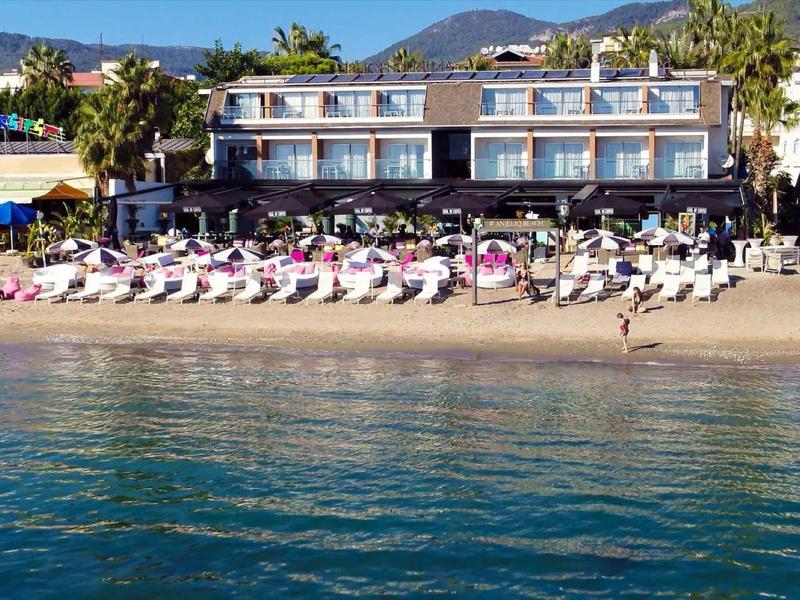 Hotel sulla spiaggia con lettini davanti e acqua limpida in primo piano.