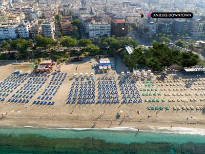 Playa con filas de tumbonas y sombrillas frente a una ciudad costera urbanizada.