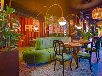 Modern eingerichtetes Café mit grünem Sofa, Holztischen, Pflanzen und hängenden Lampen.