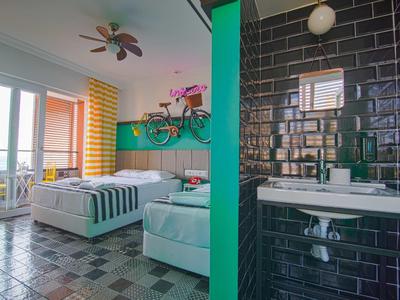 Modernes Zimmer mit großem Bett, buntem Ventilator, Fahrrad an der Wand und angrenzendem Bad.