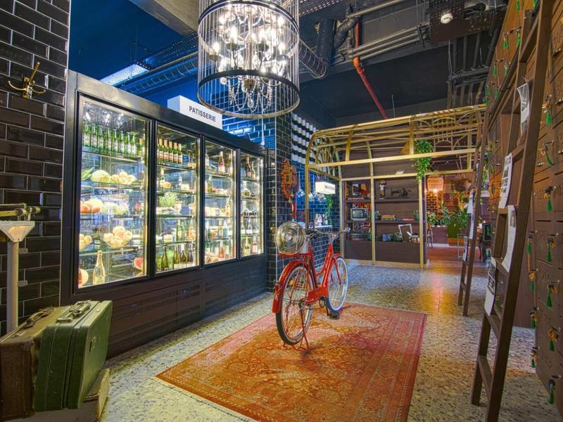 Innenraum mit Fahrrad auf Teppich, Glasvitrinen, Koffer, dunkle Wände und moderne Beleuchtung.