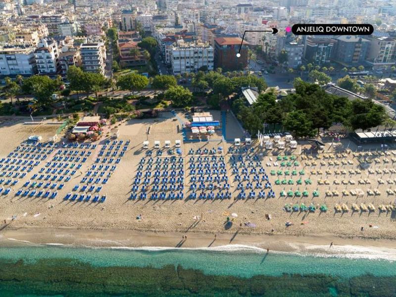 Breiter Sandstrand mit vielen Sonnenschirmen und Gebäuden im Hintergrund an der Küste einer Stadt.