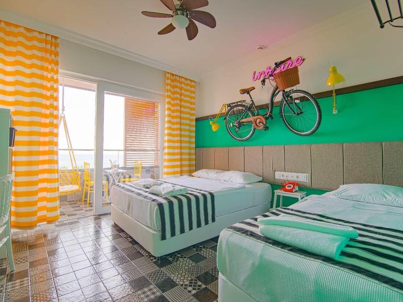 Helles Zimmer mit zwei Einzelbetten, grün-gelbem Wanddesign, Fahrrad an der Wand und Balkon mit Meerblick.