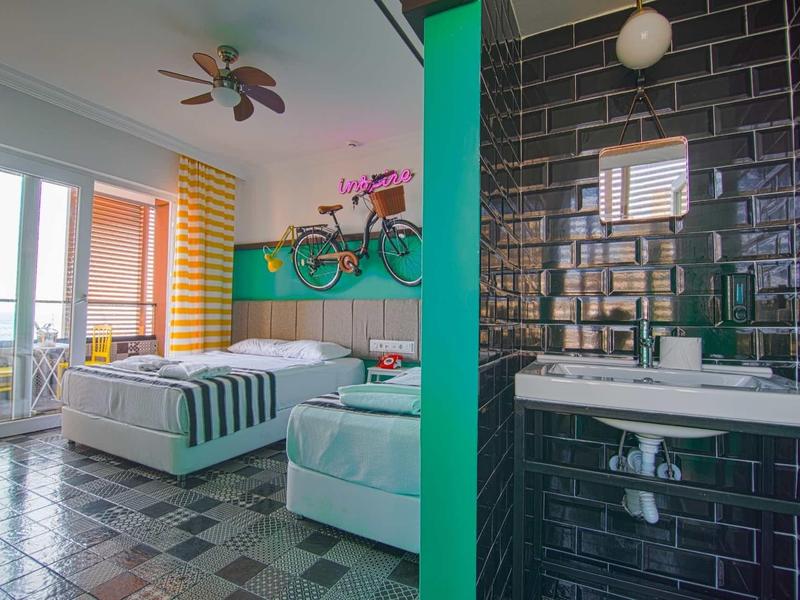 Modernes Zimmer mit großem Bett, buntem Ventilator, Fahrrad an der Wand und angrenzendem Bad.