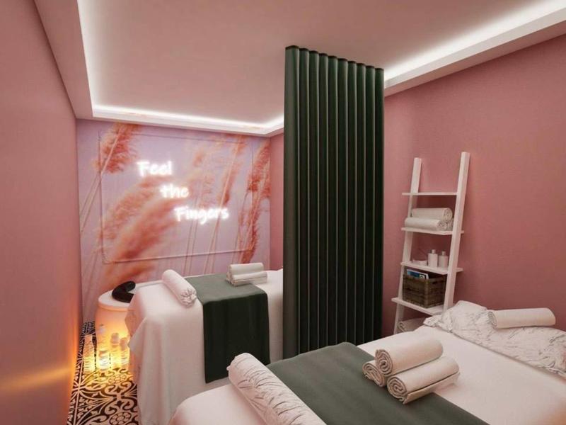 Zwei Behandlungsbetten in einem rosa Raum mit grünen Vorhängen und sanfter Beleuchtung.