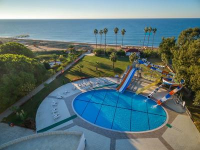 Kulatý bazén s vodními skluzavkami a výhledem na moře v hotelové zahradě s palmami.