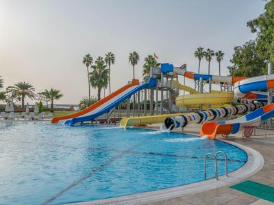 Vodní park s několika barevnými skluzavkami vedle velkého bazénu a palmami v pozadí.