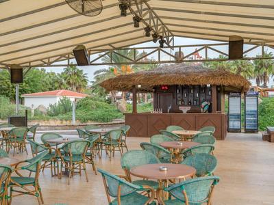 Zastřešená terasa s kulatými stoly, židlemi a barem s doškovou střechou v hotelu.