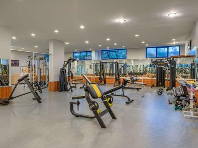 Moderní dobře osvětlená posilovna s různými cvičebními stroji a velkými okny.