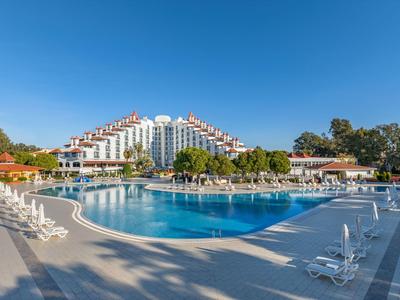 Velký venkovní bazén před moderní hotelovou budovou s deštníky a lehátky.