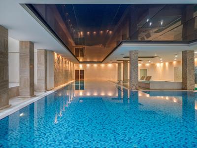 Vnitřní bazén s modrou vodou, sloupy a tlumeným osvětlením v hotelu.