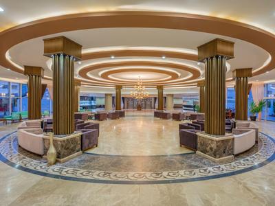 Prostorná hotelová lobby s kruhovým stropním osvětlením, sedacími oblastmi a mramorovými sloupy.