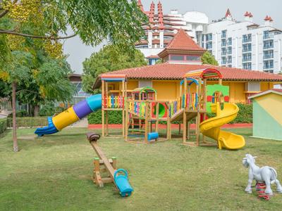 Barevné hřiště se skluzavkami a houpačkami na zelené trávě před budovami.