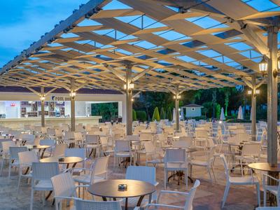 Velká zastřešená terasa s mnoha stoly a židlemi za soumraku.