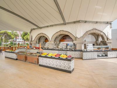 Otevřený venkovní prostor s moderním bufetem a ovocnými tácemi pod velkým bílým baldachýnem.