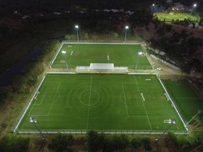 Verlicht voetbalveld 's nachts met omliggend pad en bomen