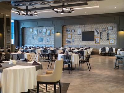 Elegancka restauracja z nakrytymi stołami, wygodnymi krzesłami i nowoczesnym oświetleniem.